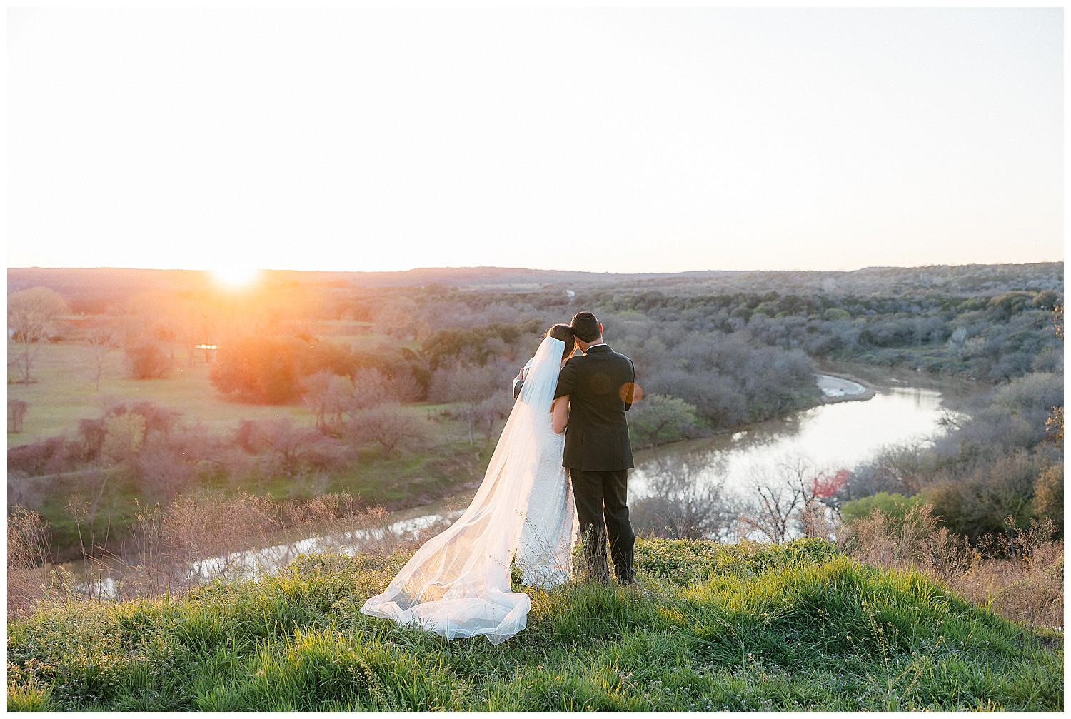 Bride and groom overlooking a sunset and river on a cliff at Rest Yourself River Ranch in Mineral Wells, TX.